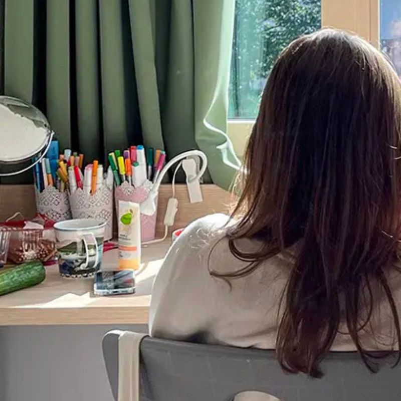 Schülerin von hinten am Schreibtisch mit dem Handy auf dem Tisch zum Thema